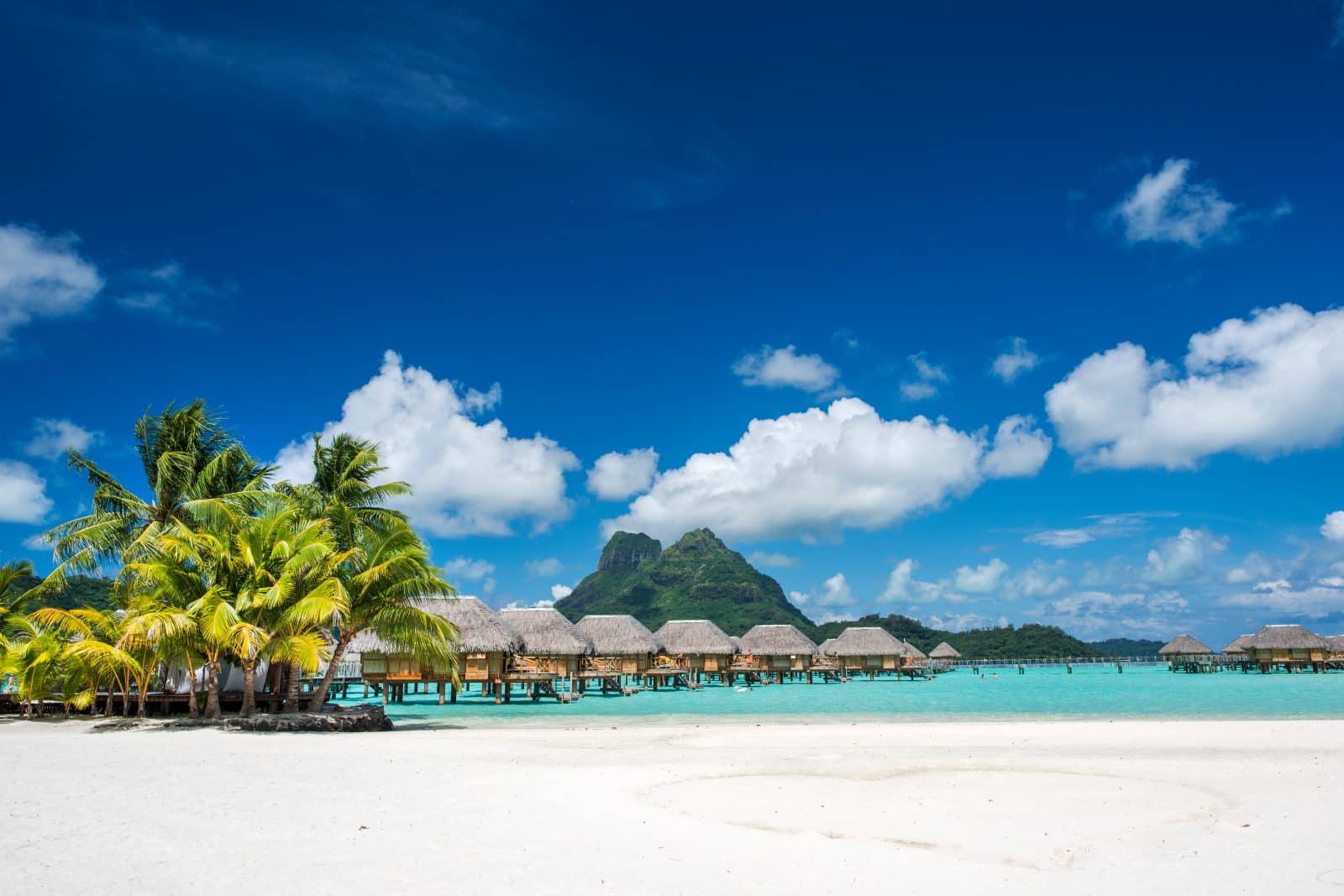 Plage de sable blanc avec hébergements sur pilotis à Tahiti